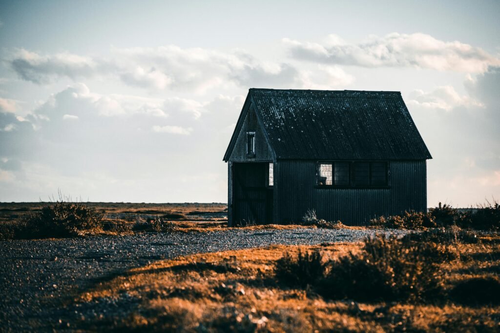 A solitary rustic cabin in a remote countryside setting under a cloudy sky.