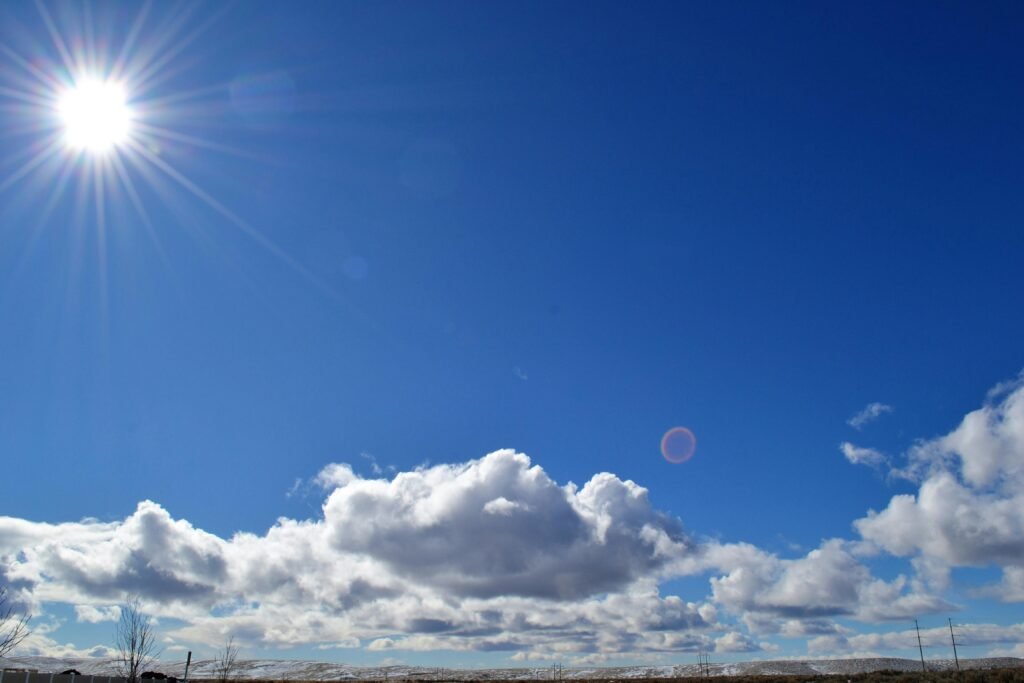 A vibrant image capturing the sun shining over fluffy clouds in a blue sky.
